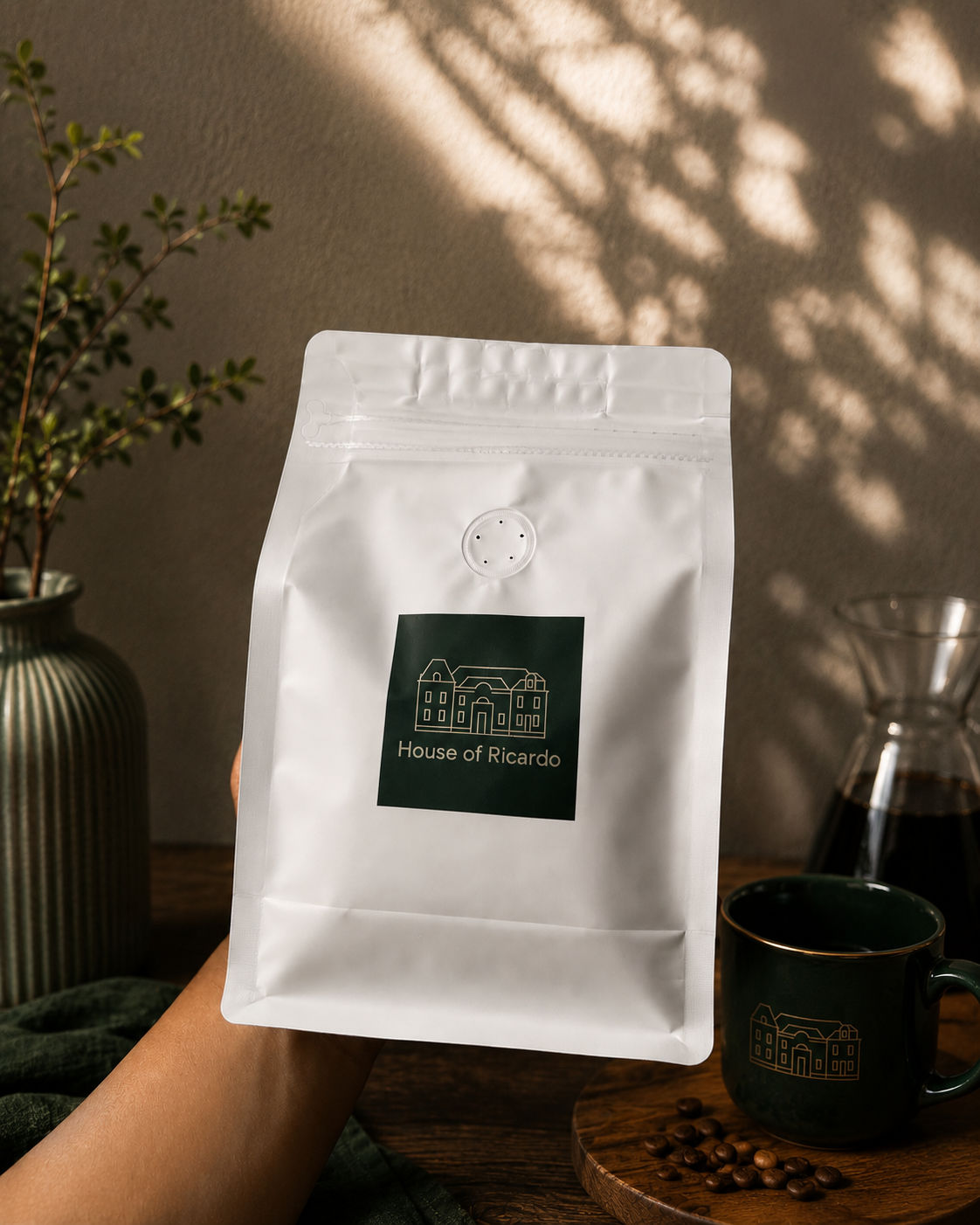 House of Ricardo bag held up beside a dark green mug and carafe